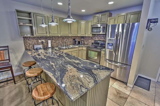 View of the kitchen with new stainless steel appliances, granite counters, docking station, Kurig, and 3-bar seats