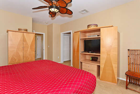 Bedroom with Entertainment Center for TV, Chair, Wardrobe, a Large Bed, and Ceiling Fan.
