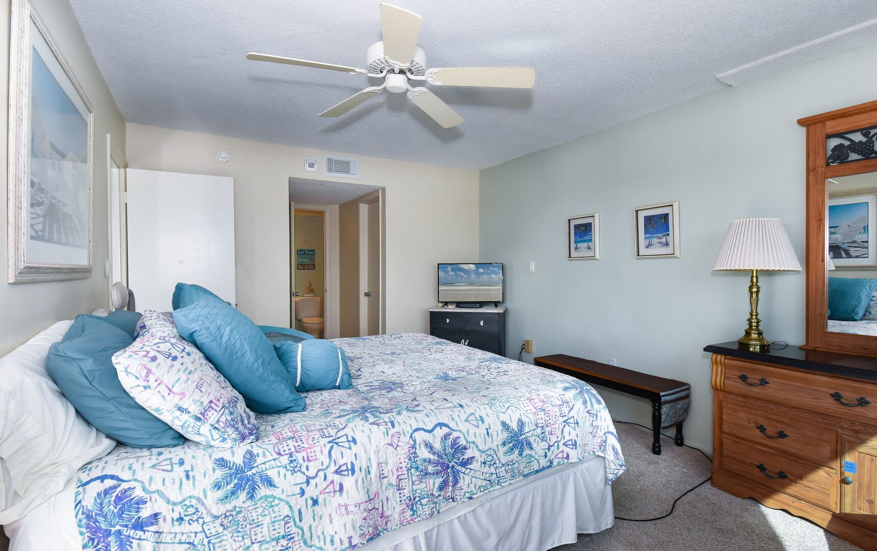 Bedroom of this private condo in New Smyrna Beach with a large bed across from a vanity dresser.