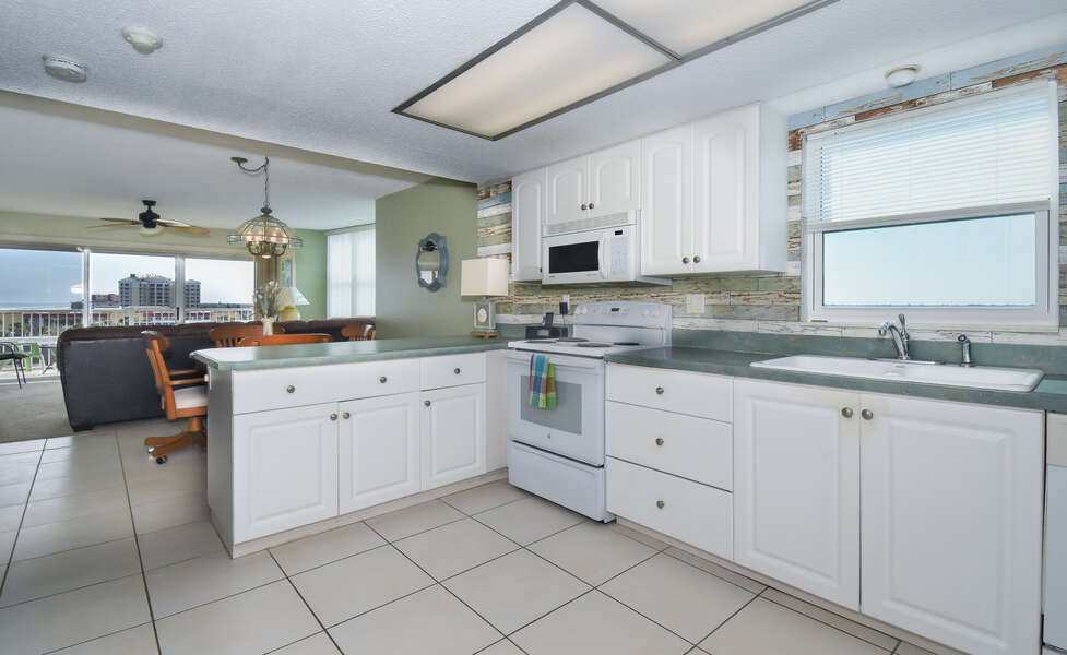 Angled photo of the kitchen, with sink, oven range, and microwave in view.
