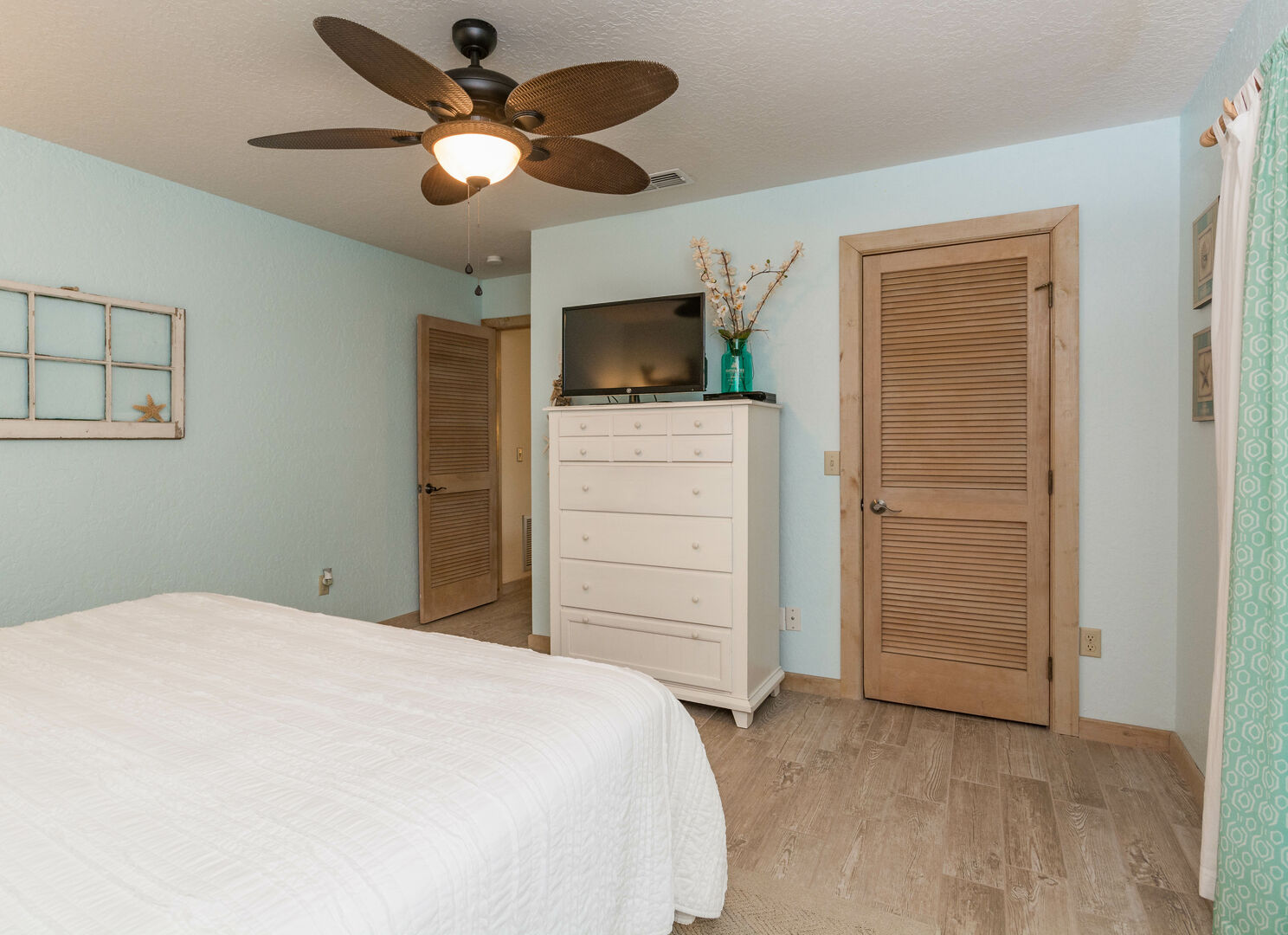 Bedroom with tall white chest of drawers and wood door featuring wood floors.