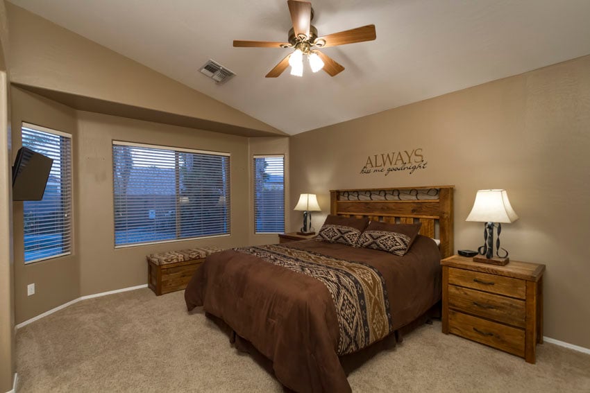 Master bedroom has a queen bed, bay windows overlooking pool, ceiling fan and two tables with lamps.