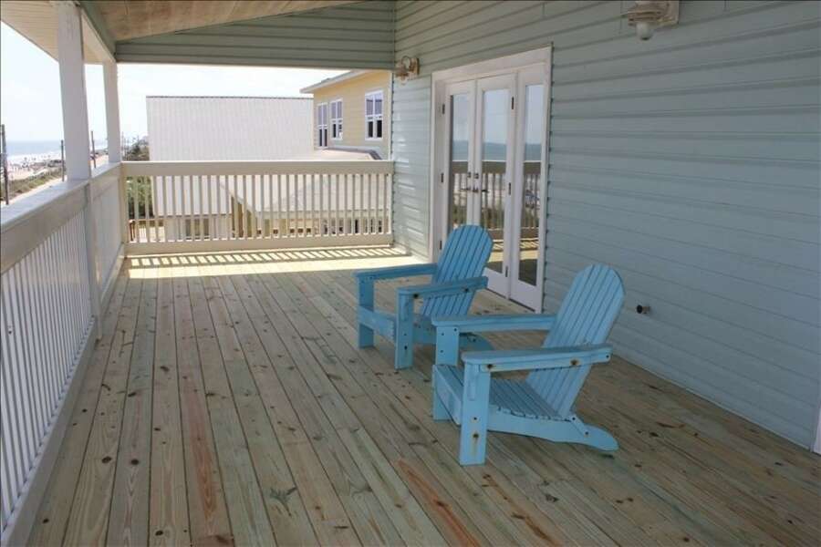 Two blue reclining chairs on wood patio with white fencing.