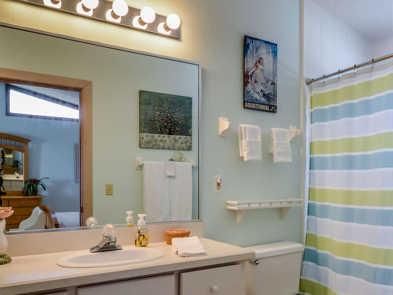 Bathroom with green and blue striped shower curtain and extra large framed mirror.