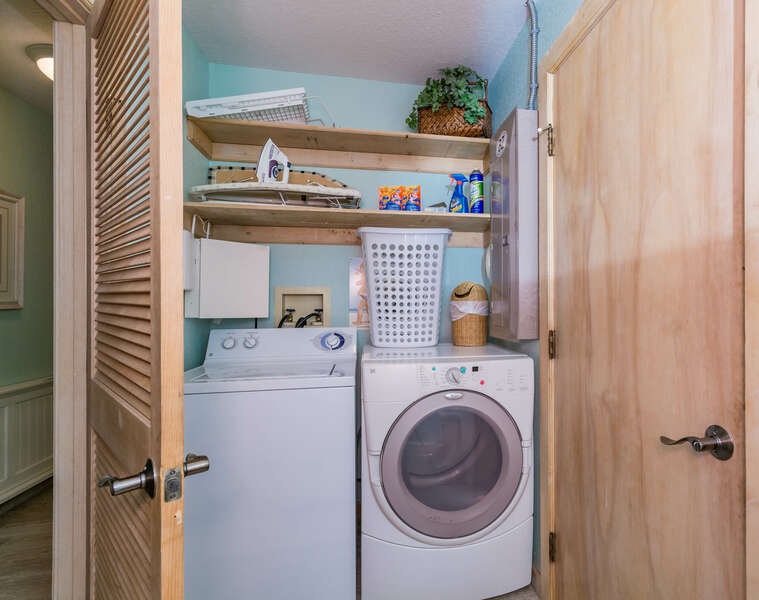 Laundry room with full-sized washer and dryer topped by floating shelves and laundry supplies.