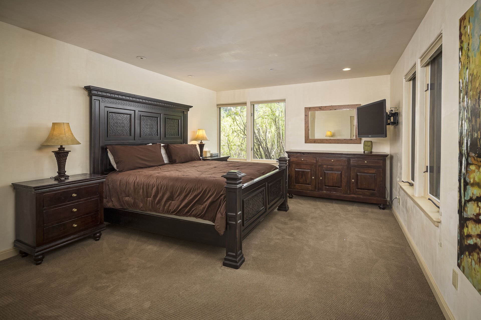 Twin nightstands on either side of a large bed in a bedroom, complete with a wall-mounted TV and vanity dresser.