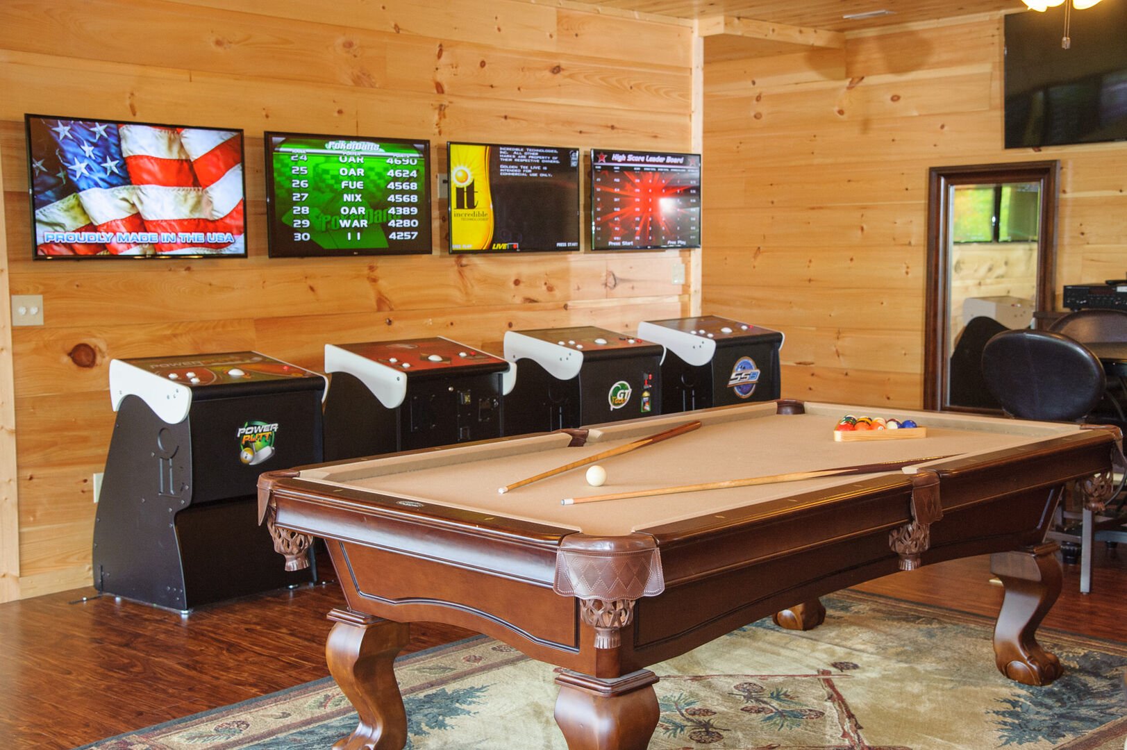 Pool table in front of arcade cabinets with wall-mounted screens.