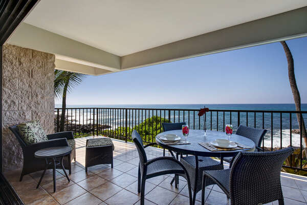 Ocean Front Lanai of this Kona Hawai'i vacation rental with cushioned chairs and a set table.