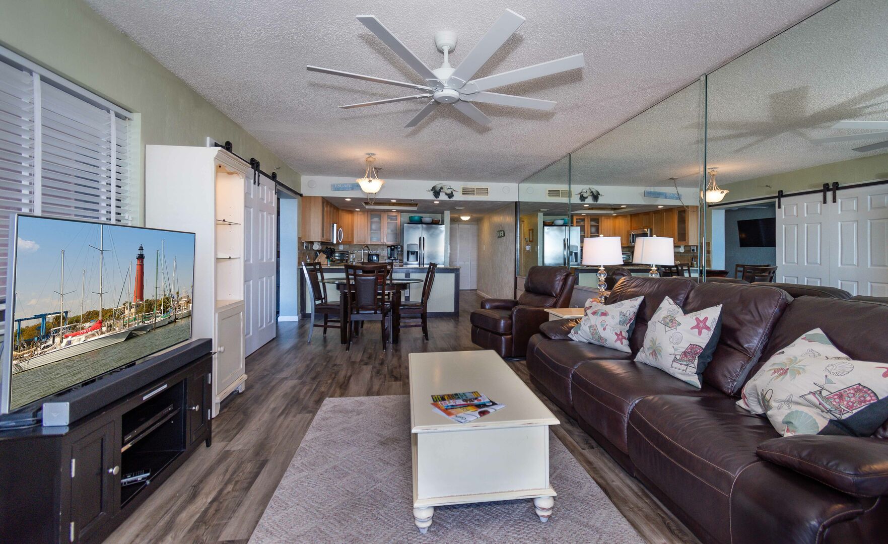Living area of this vacation condo in New Smyrna Beach with flat screen TV, couch, and mirror wall.