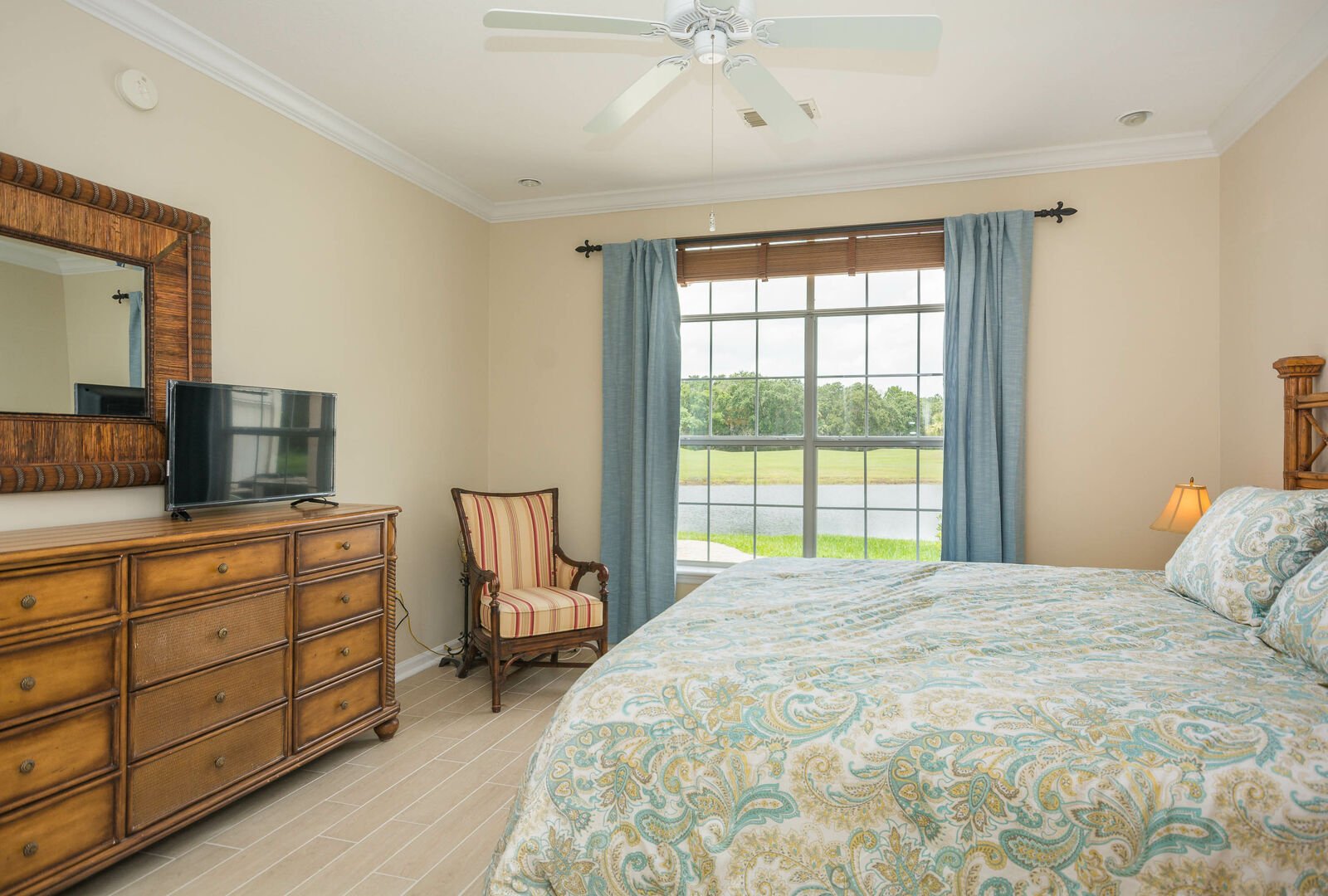 A flat-screen TV on the dresser in front of the bed, and large windows with a view of the pond and golf course.