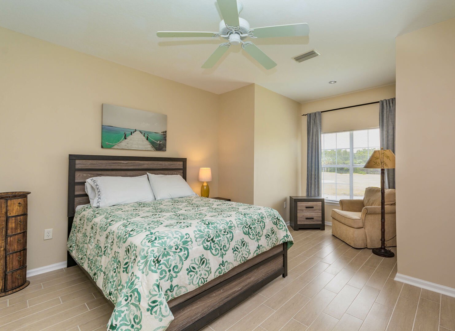 2nd bedroom of this New Smyrna beach Florida vacation home with a queen-sized bed, armchair, and nightstand.