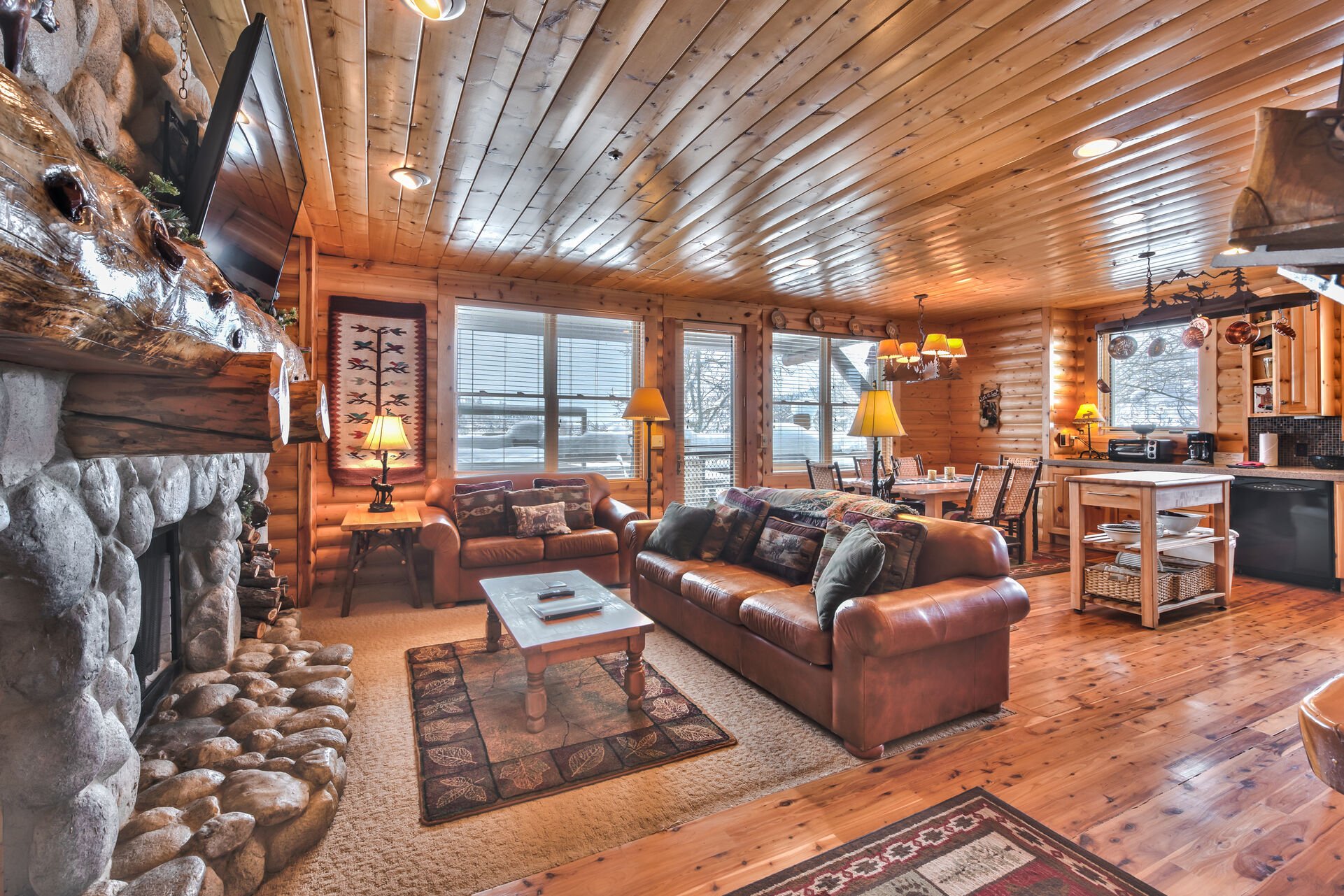 Log Cabin Design Condo with Great Room featuring a Living Room with a Stone Fireplace, Fully Equipped Kitchen, Dining Area, Hardwood Floors, and Private Deck