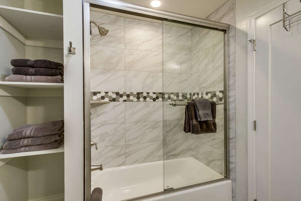 Shower-Tub Combo with Glass Doors and Storage Shelves.
