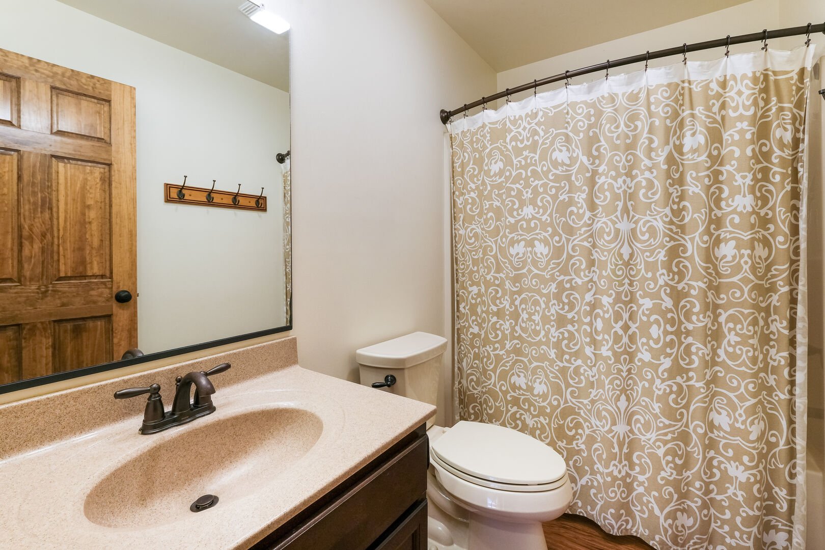 Toilet, sink, and shower of bathroom, with curtain closed and door visible in the sink mirror.