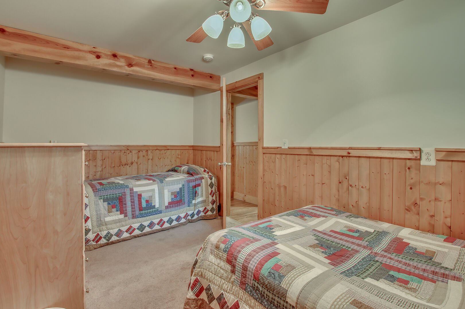 A quilt covered bed, couch, and the ceiling fan in one of this homes bedrooms.