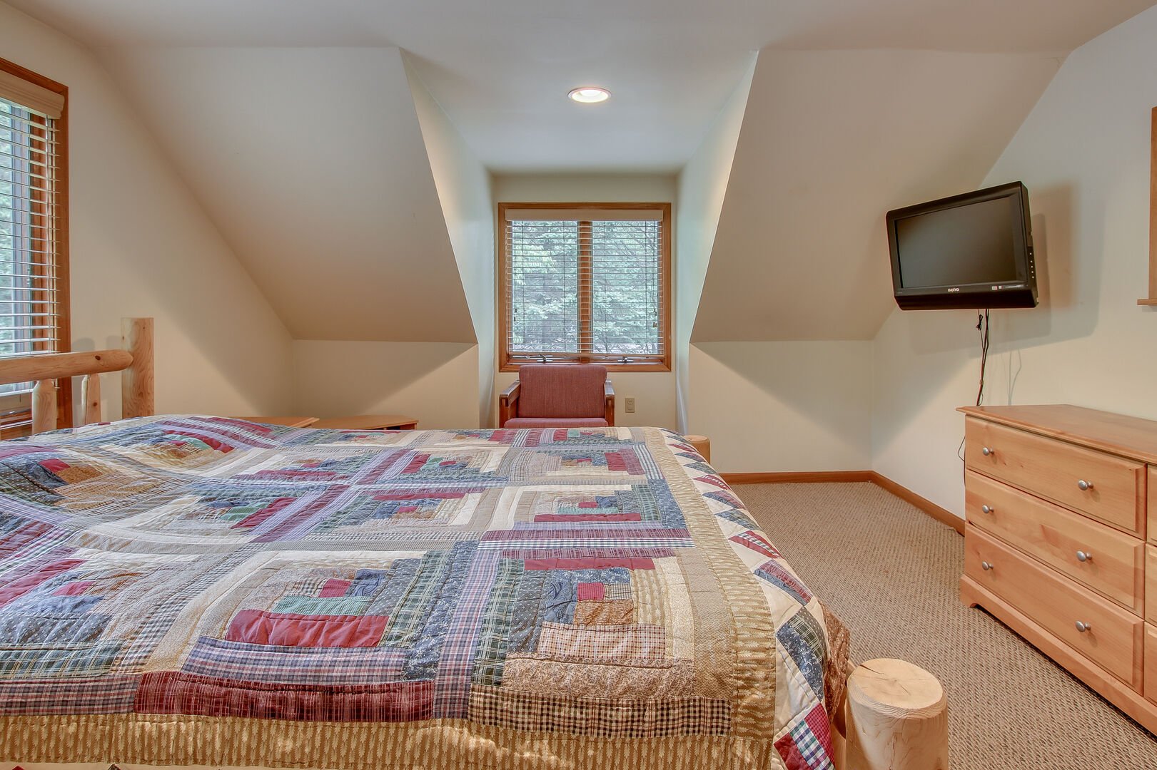 The master bedroom of this Pocono rental in Towamensing Trails, with bed, dresser, armchair, and TV.