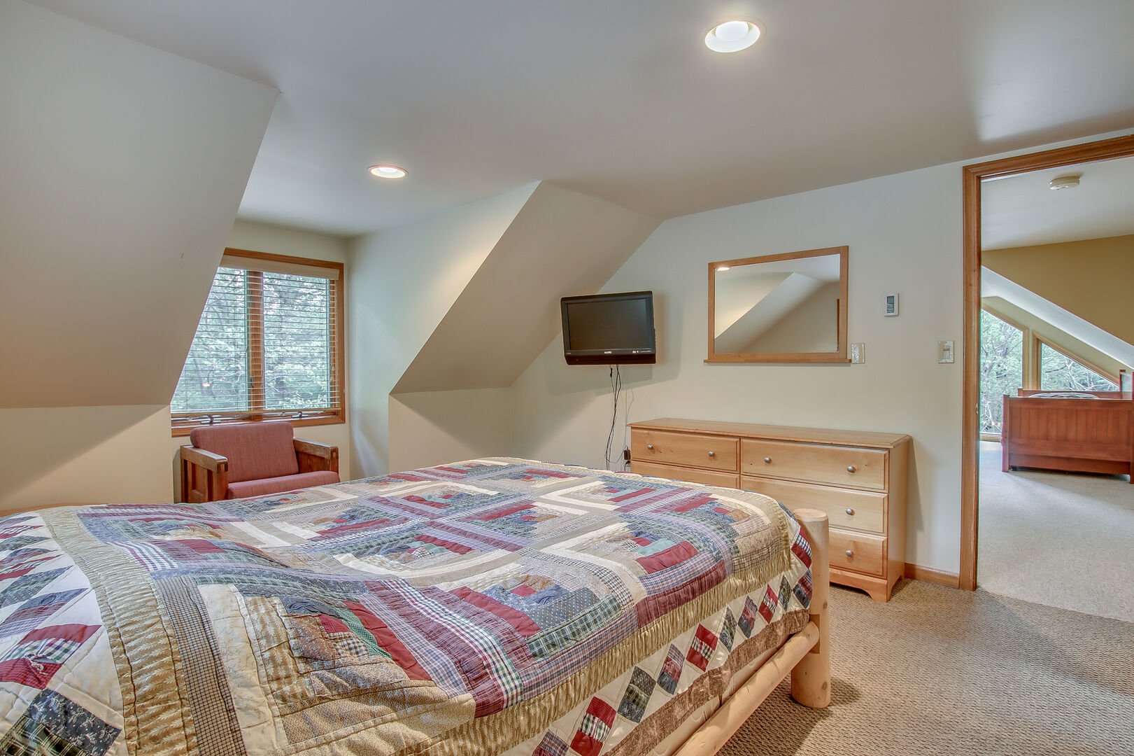 Another shot of the master bedroom of this Pocono rental in Towanmensing Trails, with a bed, armchair, dresser, TV and Mirror in shot. The door opens to upper floor.