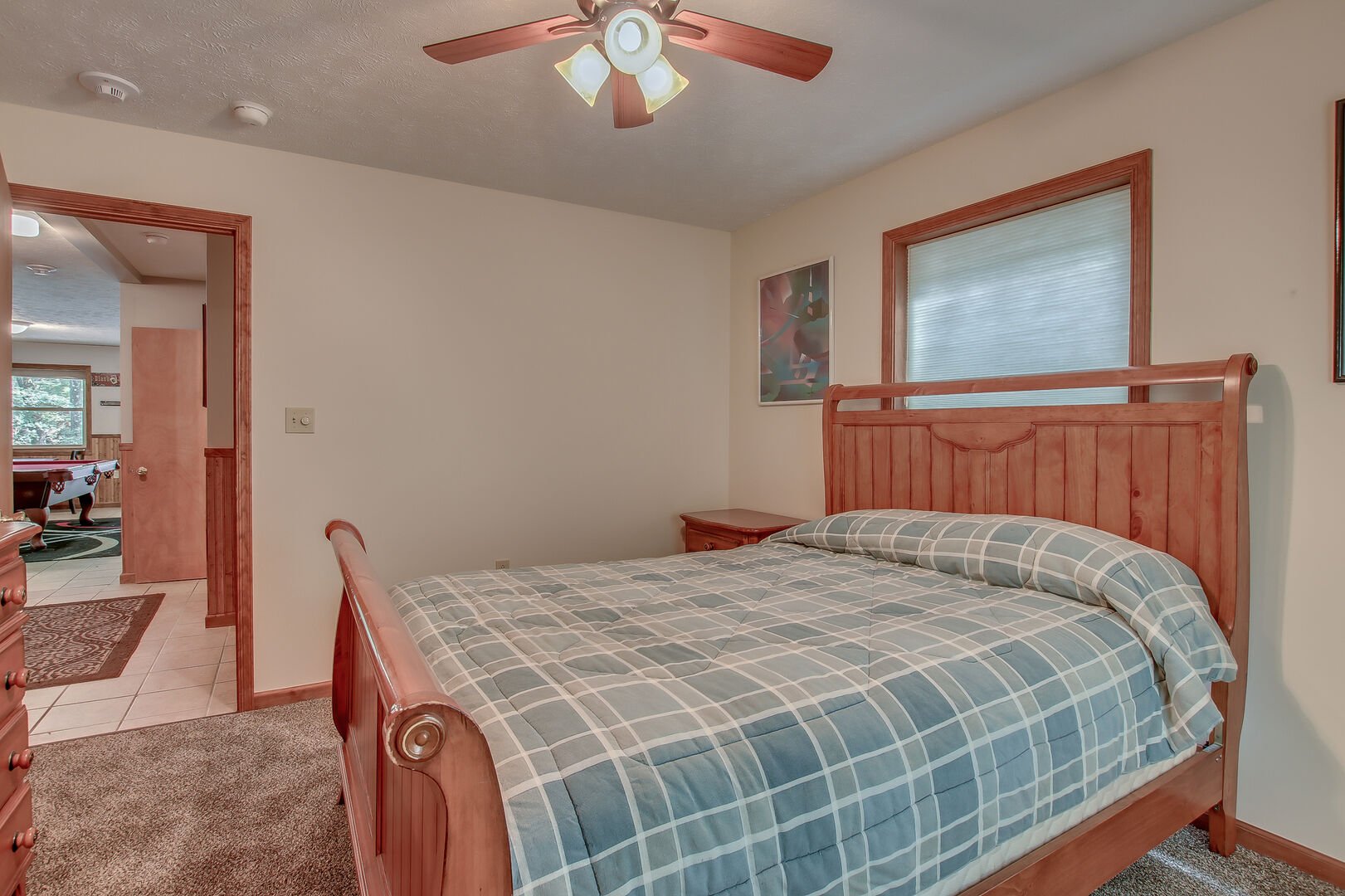 A picture of a bed in the center of a bedroom, with a door open to the game room of this Lake Harmony rental.