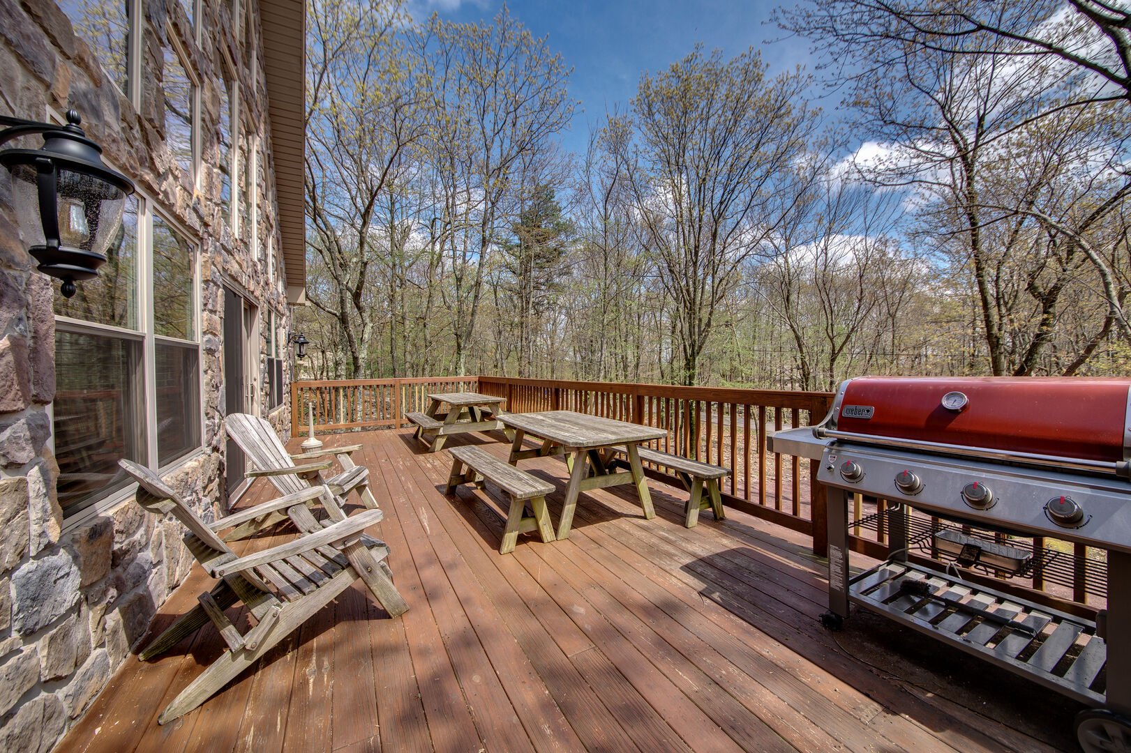 A Large Deck With Adirondak Chairs, Picnic Tables, and a Gas Grill.