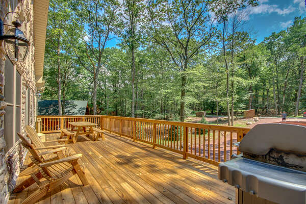 Front porch with picnic table, patio chairs, and grill overlooking  forest scenery.