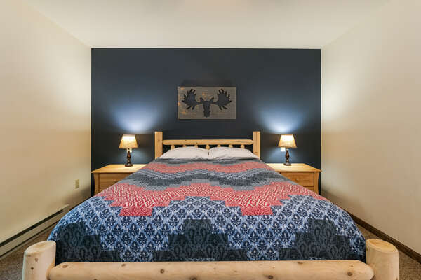 Bed with moose painting over it, nightstands on either side.