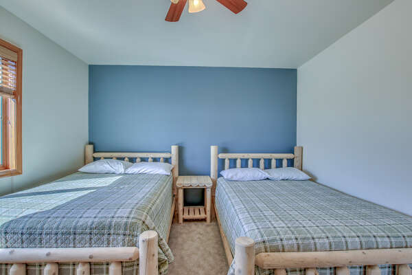 Two Wooden Beds Featured in Bedroom with Dark Blue Accent Wall.
