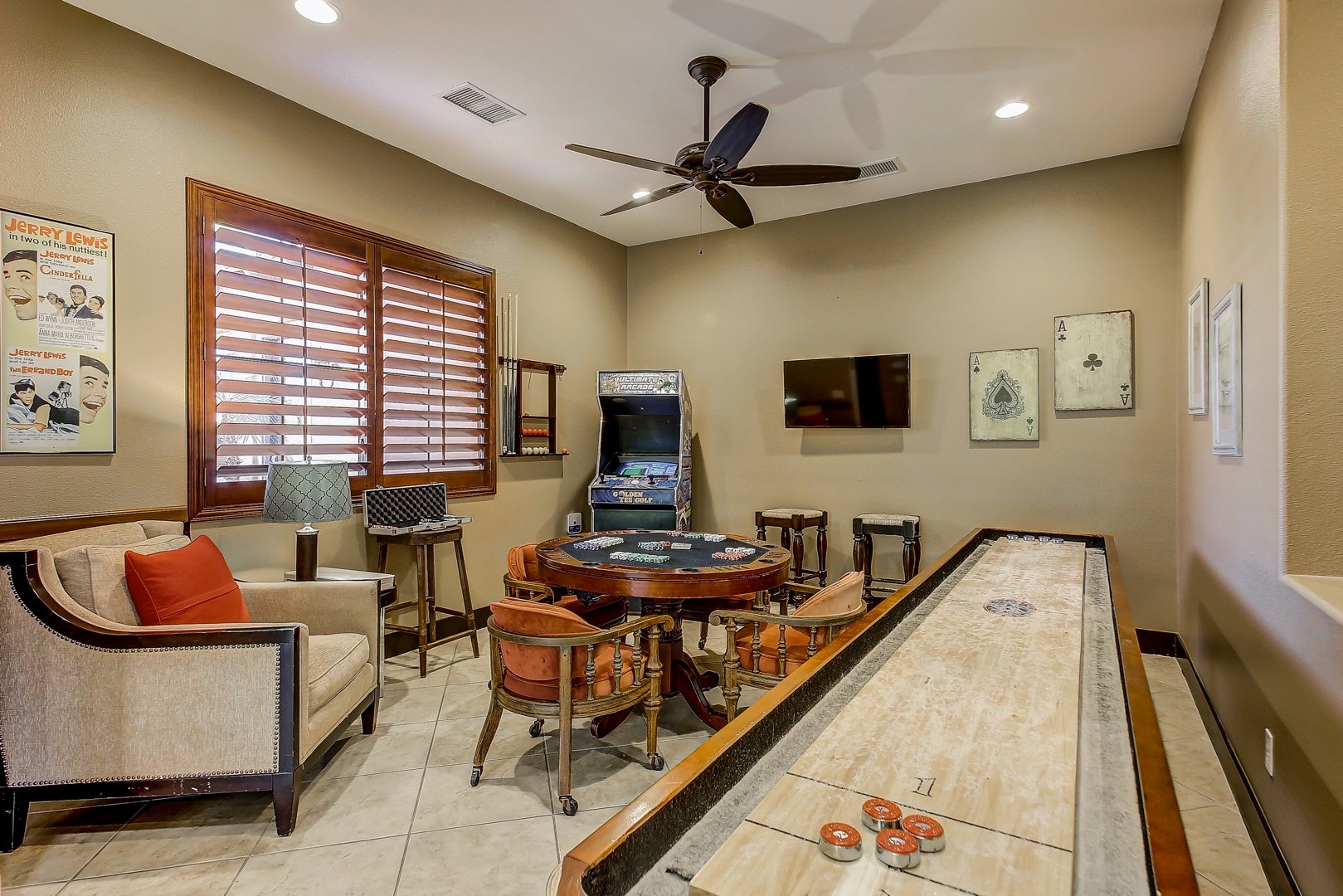 Man cave type game room with shuffleboard, stand up retro 80's video game machine, TV, poker table, and more.