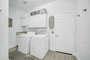 Fully equipped laundry room with washer, dryer, ironing board, iron, and laundry pods.