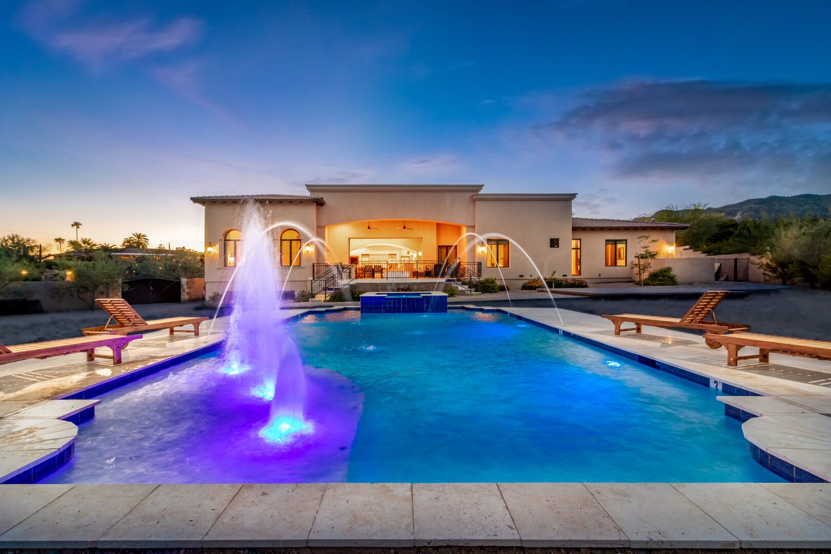 The luxury pool of this vacation home rental in Phoenix, with water features and pool chairs along the sides.