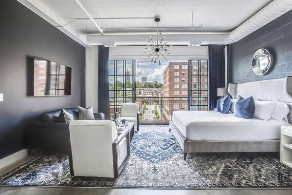 Living/Sleeping area of this Apartment Near Ponce City Market, complete with large bed, sofa, armchairs, and a small table in front of a large open window.