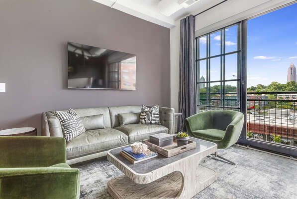 Living area of this Ponce City Flat, with a wall-mounted TV, sofa, armchairs, and coffee table in front of a large open window.