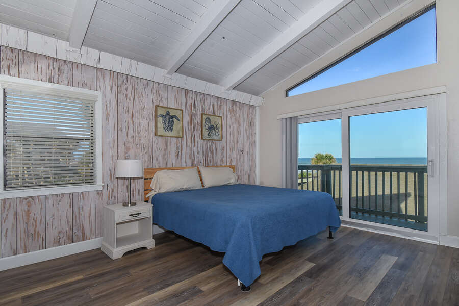 Large bedroom with king bed covered in blue with large doors facing ocean