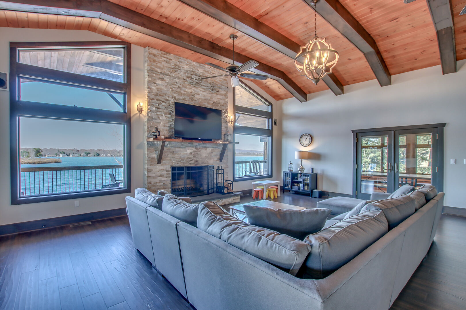 Great room with sectional couch, TV, fireplace, and large windows overlooking the lake.