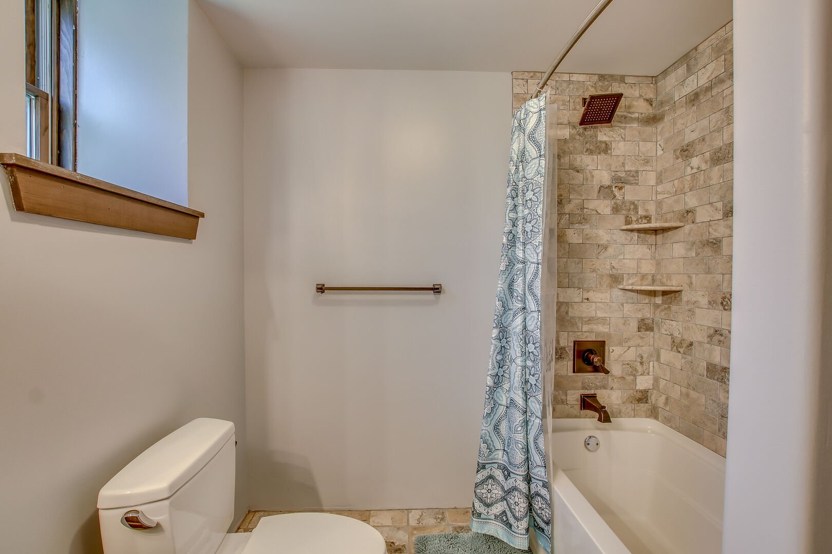Bathroom with tiled shower with the curtain open and a toilet in the bottom left.