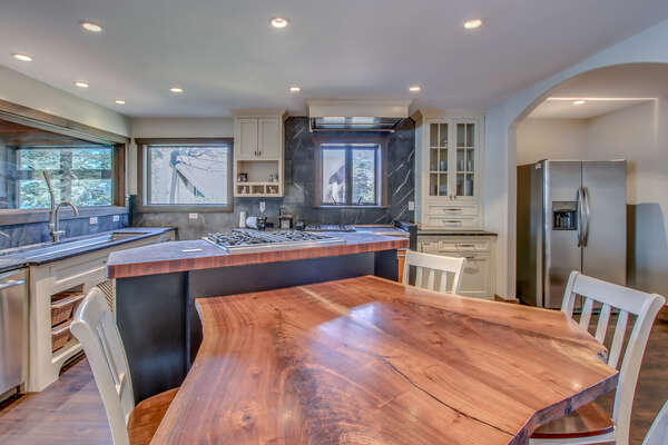 The unique wood table of the kitchen, with chairs around it, beside the kitchen island and sink in the background.