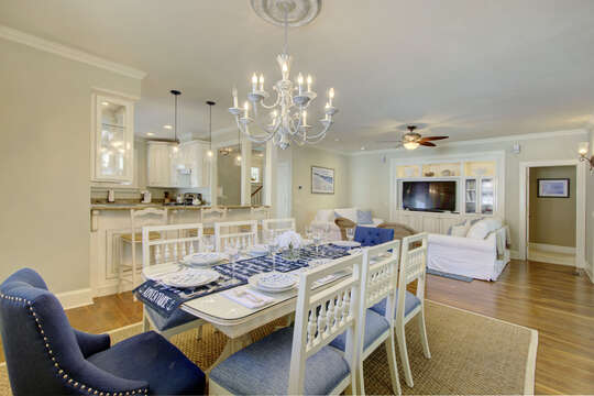 Dining area with long table, chairs, and views of the kitchen and living area.