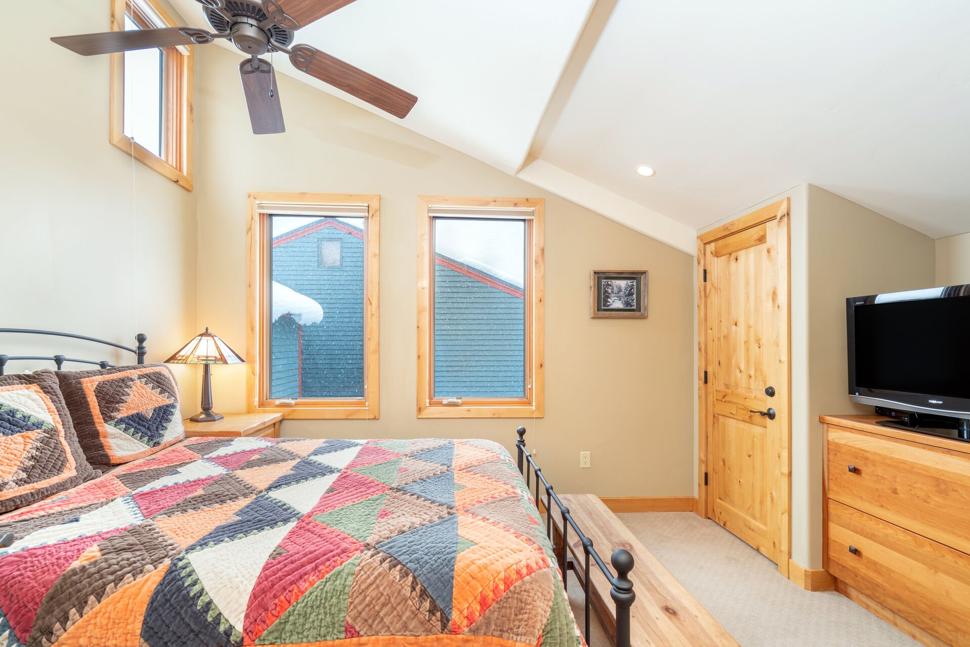 Bedroom of this 2 bedroom condo in Telluride with ceiling fan, dresser, and TV around a large bed.