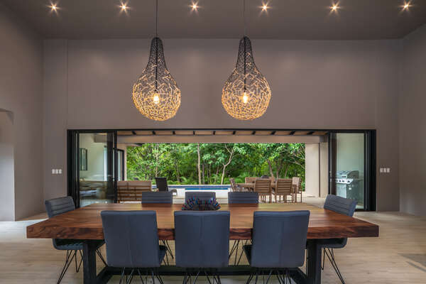 The beautiful lamps cast a soft glow over a lovely wooden dining table, surrounded by comfy chairs.