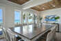 The dining area boasts a large dining table, chairs, and large windows looking out onto the ocean.