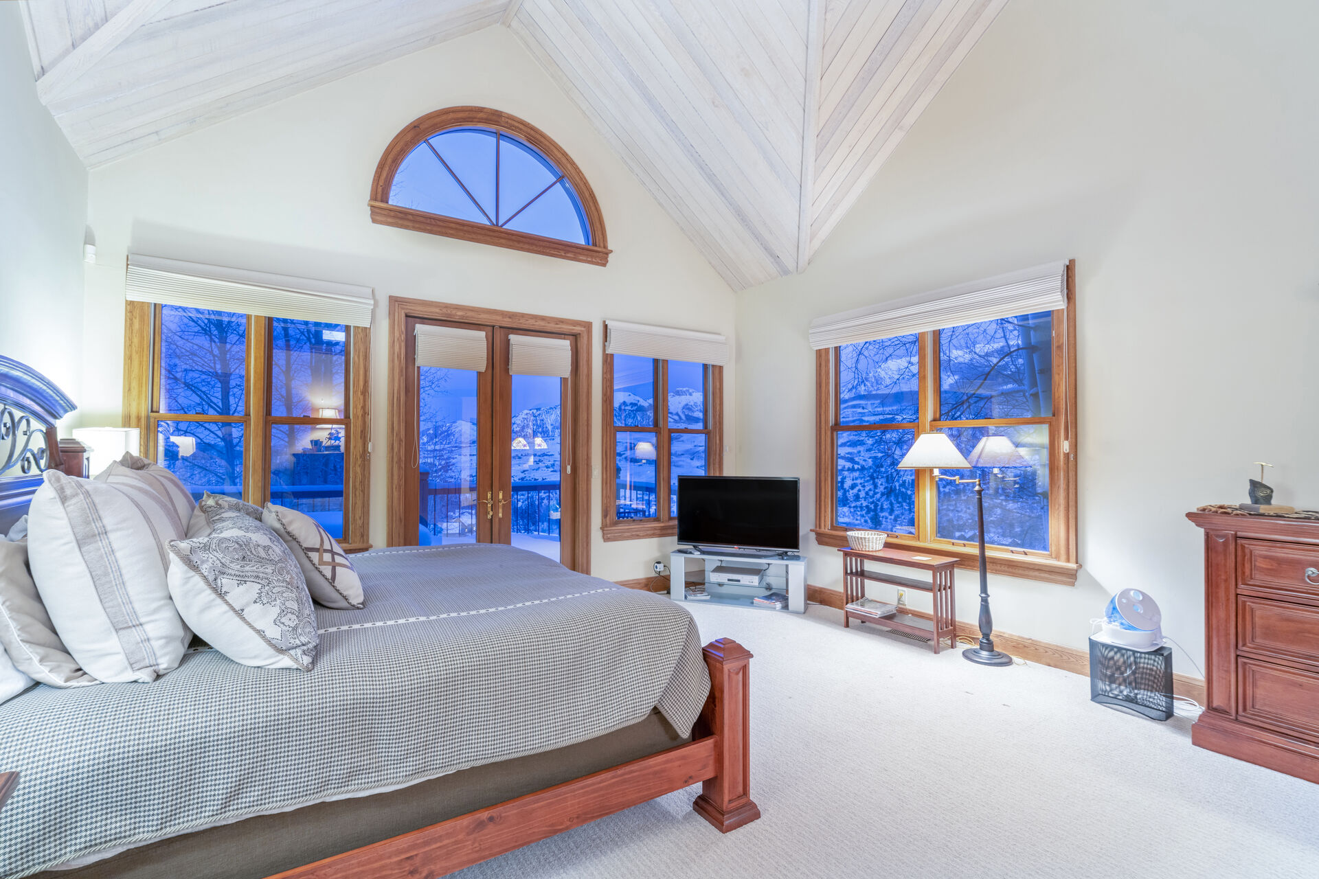 Master bedroom with ample floor space, flat-screen TV, and large bed, all surrounded by large windows.