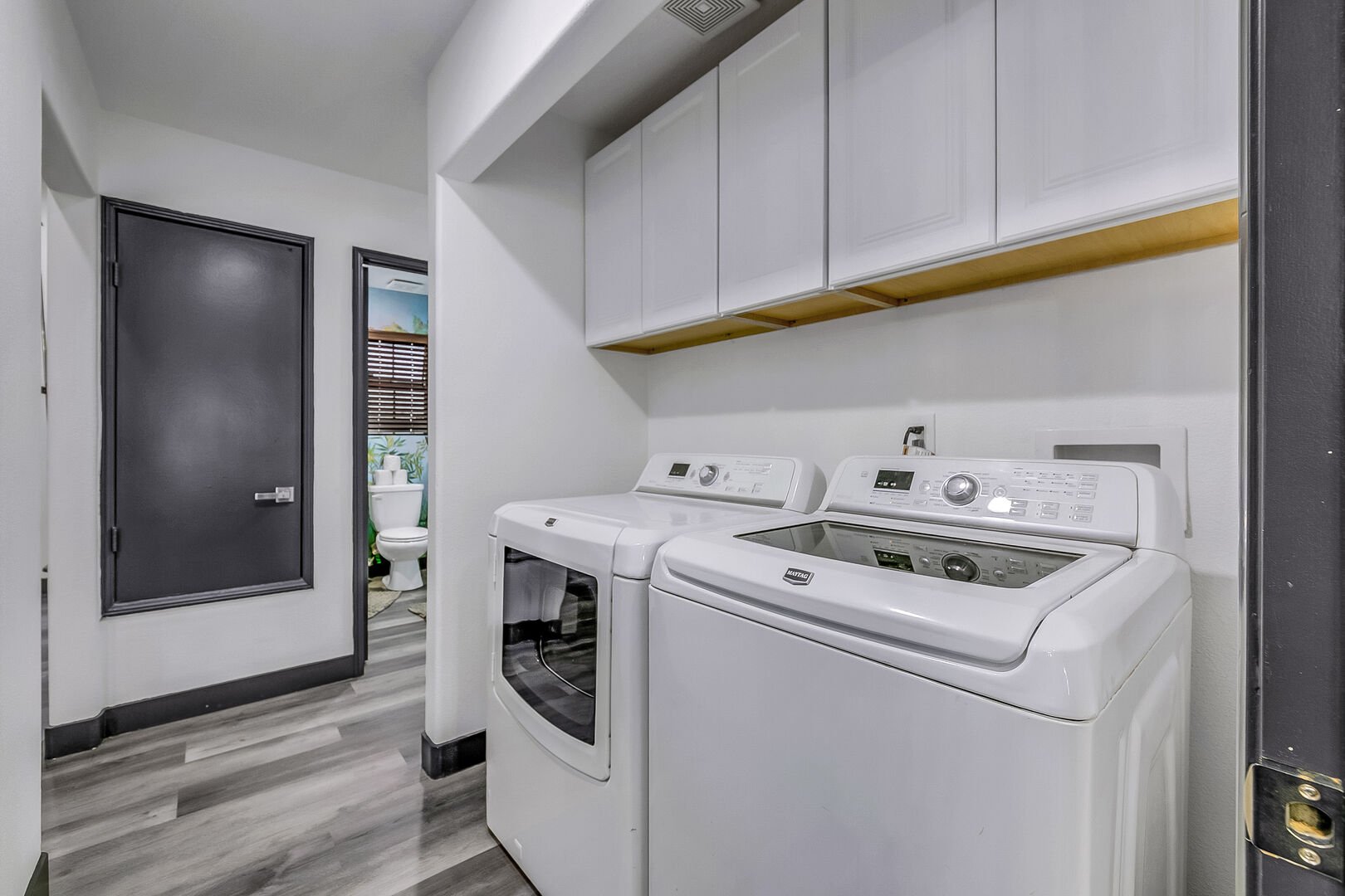 The fully equipped laundry room with washer, dryer, ironing board, iron, and laundry pods.