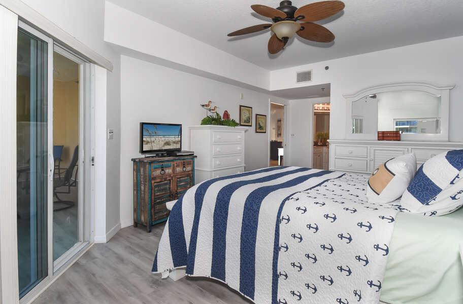 Large bed, ceiling fan, dresser, smart TV, and sliding doors to the balcony