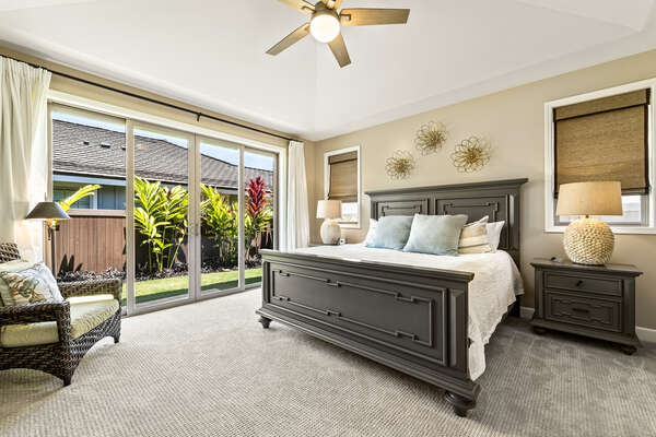 The main bedroom of this Holua Kai at Keauhou rental with King bed, personal armchair, and sliding glass doors outside.