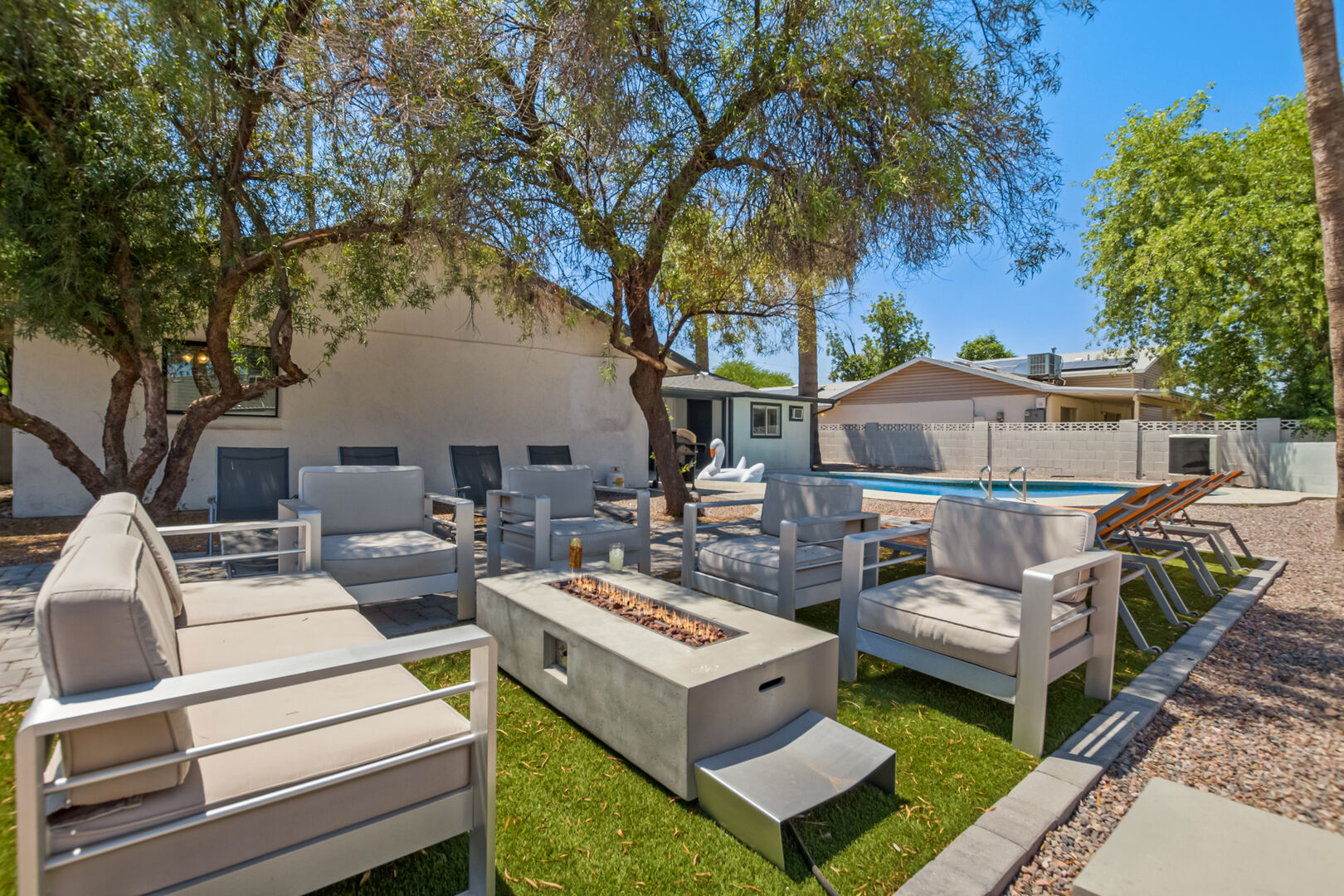 Private Backyard Oasis featuring a sparkling blue pool, sun loungers, covered patio, firepit with outdoor furnishing.
