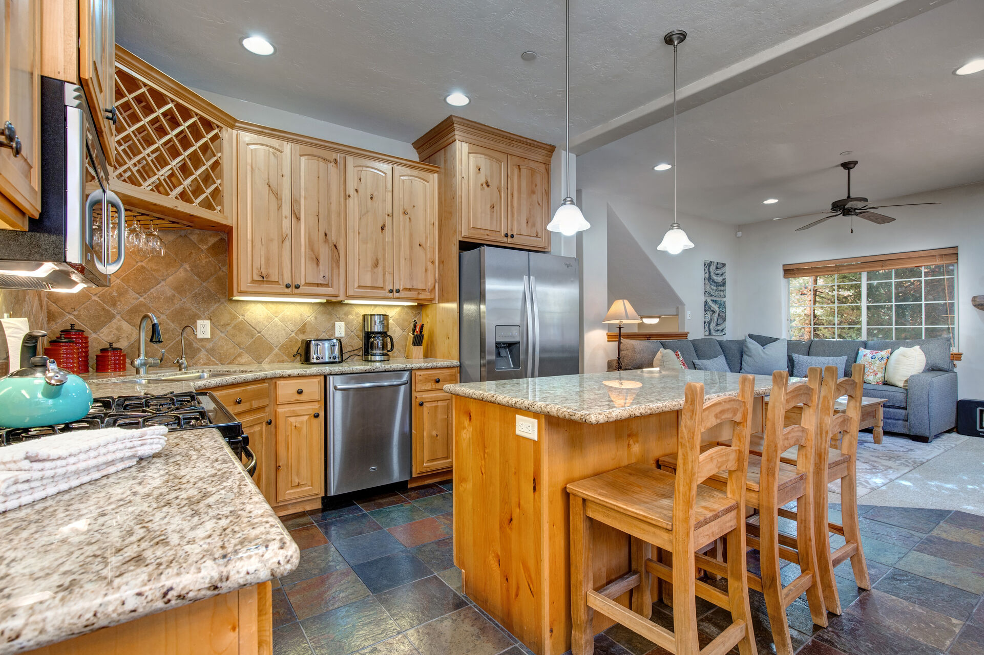 Fully Equipped Kitchen with stone countertops, island seating for three, wine rack, stainless steel appliances, and icee maker