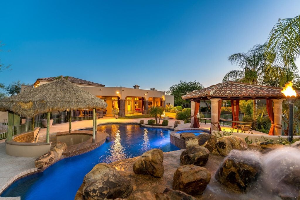 Tropical Resort style backyard featuring a heated sparkling blue pool and hot tub with a waterfall, built-in bar, and a covered terrace offering outdoor dining.