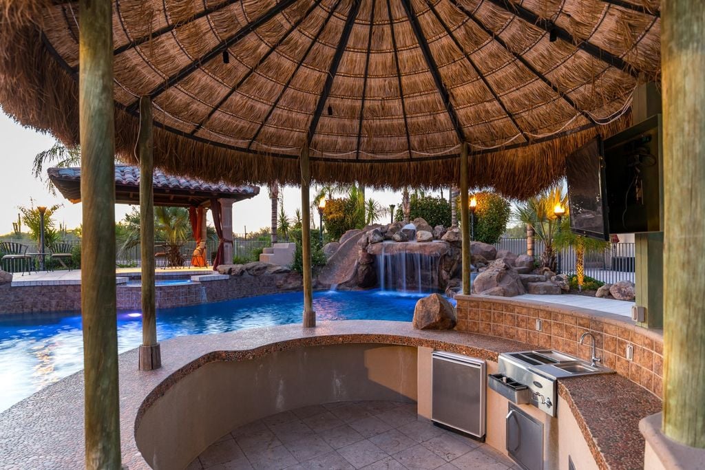 Tropical Resort style backyard featuring a heated sparkling blue pool and hot tub with a waterfall and built-in bar.