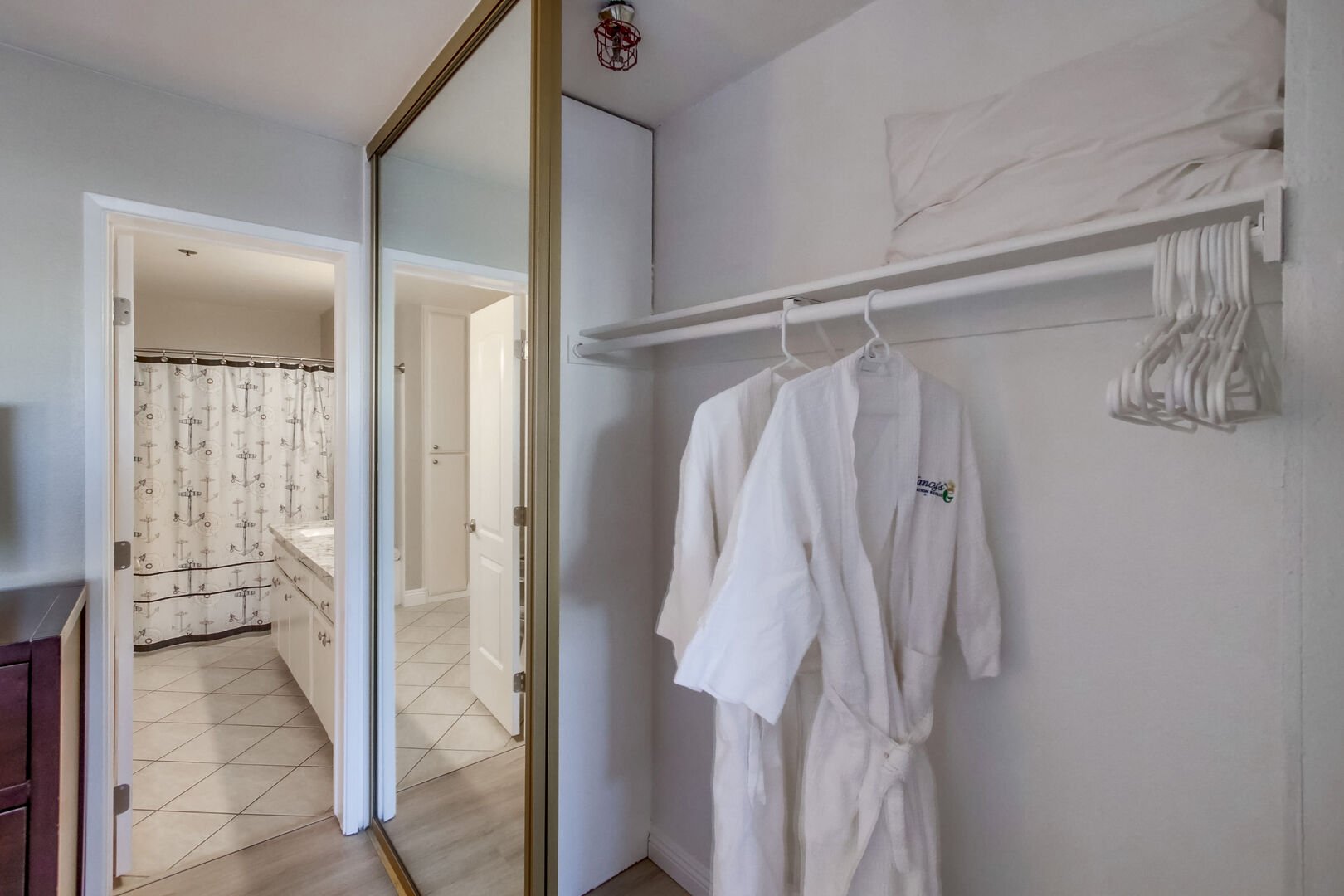 Entrance to in-suite full bathroom with peek into large mirrored closets with guest robes and hangers