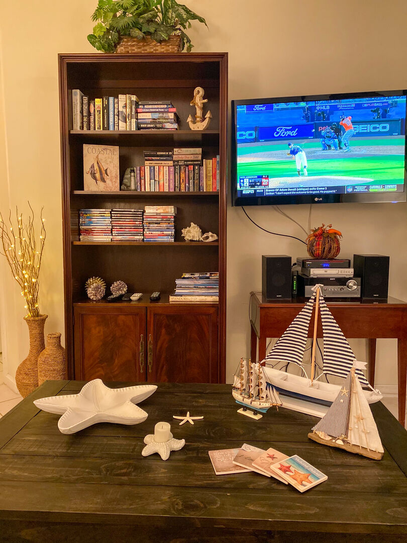 Living room with bookshelf, coffee table, TV, and beachy sailing decor