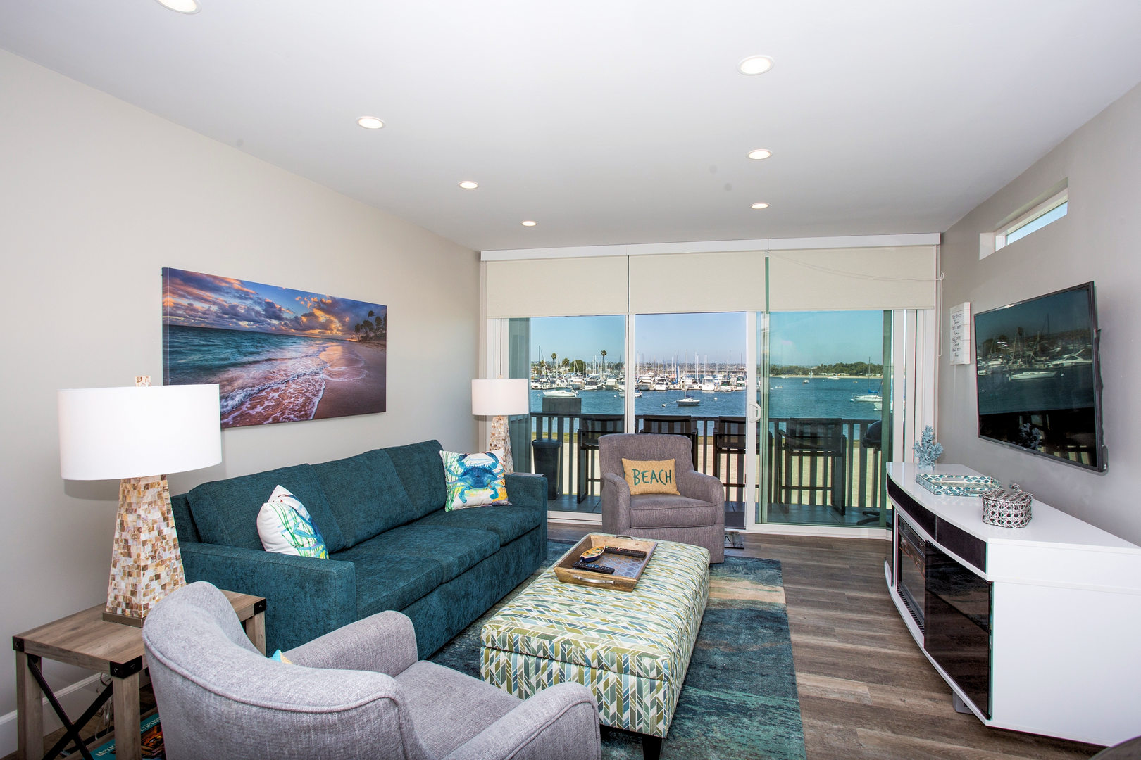 Living room with flat screen TV, floor to ceiling windows, private balcony and a view of the bay